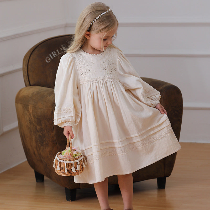 Little girl in cream lace dress holding flower basket, vintage armchair, indoor setting